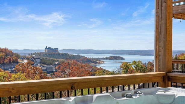 A hot tub on a wooden deck overlooking a lake with autumn foliage and a distant castle. - Gorgeous Lake View! Indoor Pool! 5 Min to Branson Strip! (Branson)