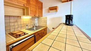 Une cuisine compacte avec des meubles en bois, un dosseret carrelé, un évier et une machine à café posée sur le plan de travail.