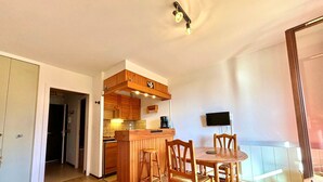 Un espace de vie compact comprenant un coin cuisine, un coin repas et un téléviseur fixé au mur.
