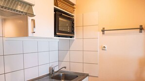 A compact kitchen with white tiles, a stainless steel sink, a stove, and an oven.