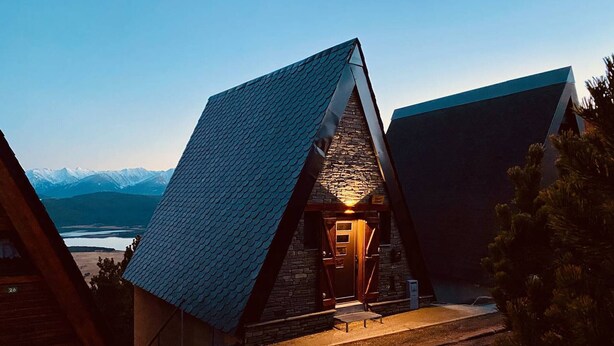 A modern, triangular-roofed building with a stone facade and a wooden door, set against a mountainous backdrop. - Cozy chalet with jacuzzi and lake views (Les Angles)