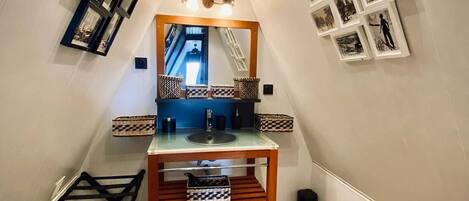 A narrow hallway with a wooden bench, a mirror, and a sink.