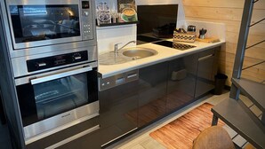 A modern kitchen with stainless steel appliances, a sink, and wooden cabinetry. - Cozy chalet with jacuzzi and lake views (Les Angles)