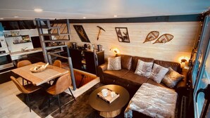 A modern living room with a sofa, coffee table, and dining area. There is a kitchen in the background with a ladder and various kitchen items. - Cozy chalet with jacuzzi and lake views (Les Angles)