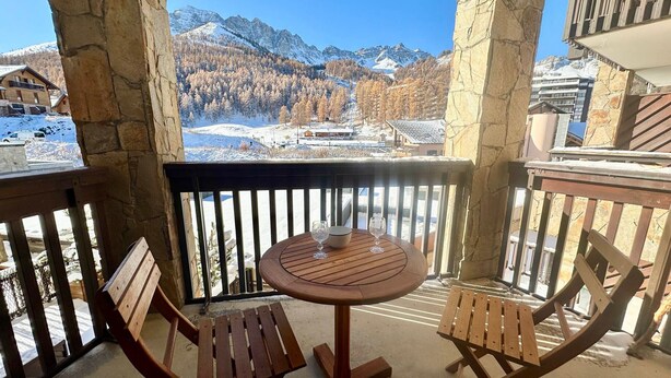 A wooden table and two chairs on a balcony with a stone wall, overlooking a snowy mountain landscape. - Apartment Vars, 2 bedrooms, 4 persons (Vars)