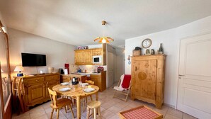 A compact kitchen with wooden cabinets, a dining table with chairs, a small stool, a television, and a microwave. - Apartment Vars, 2 bedrooms, 4 persons (Vars)