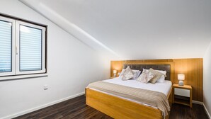 Un dormitorio con una cama de madera, dos mesitas de noche con lámparas, una ventana con persianas y un techo inclinado.