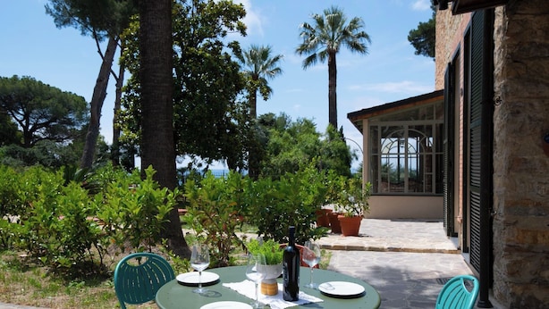 An outdoor dining area with a table set for two, surrounded by greenery and a view of the sea.