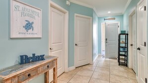 Un couloir aux murs de couleur turquoise, aux portes blanches et orné d’une console en bois sur laquelle est disposé un objet décoratif avec l’inscription « Relax ».