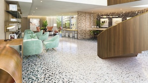A spacious lobby with a high ceiling, a central seating area with chairs, a reception desk, and a staircase leading to an upper level.