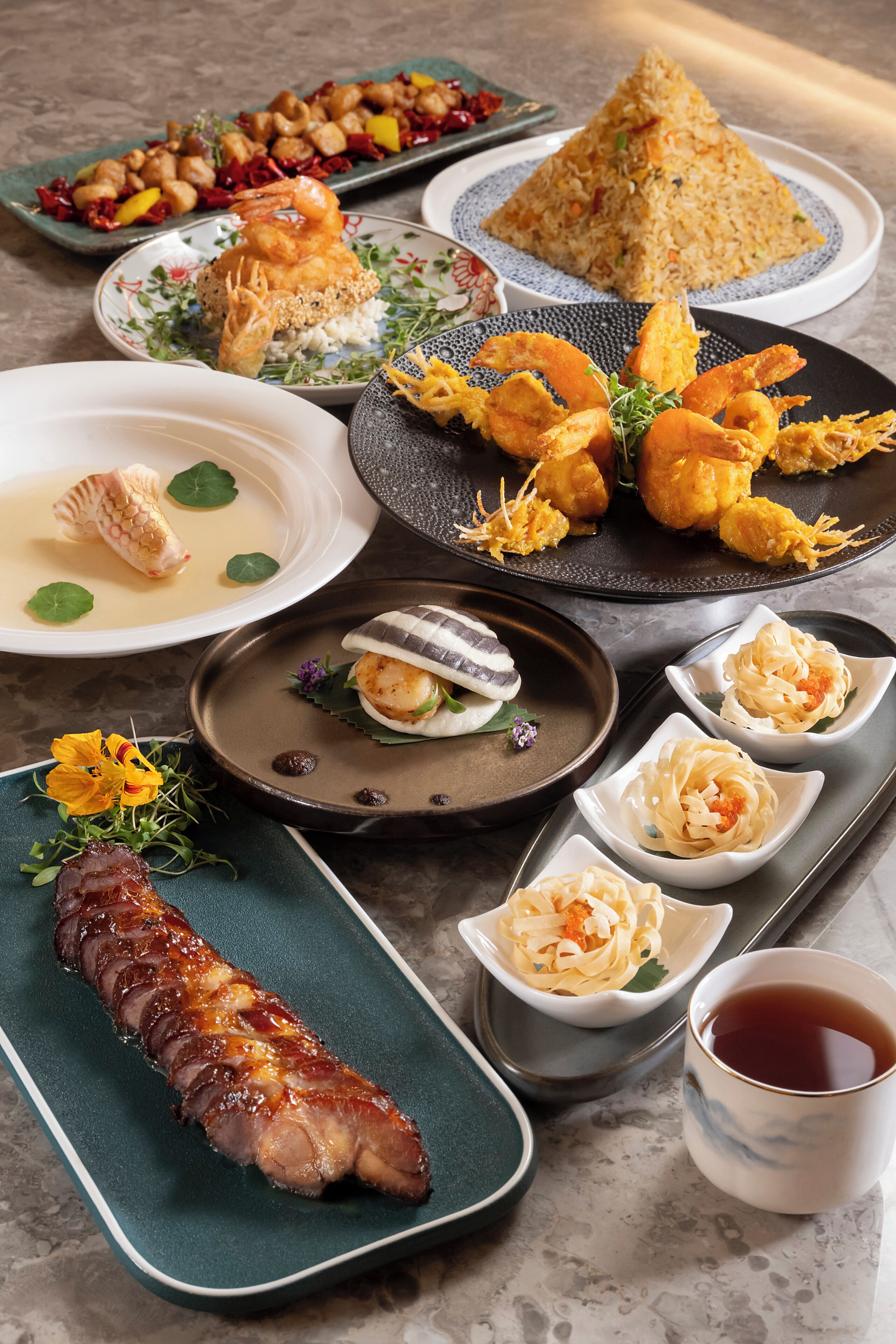 A variety of dishes including fried shrimp, rice, and a seared fish, presented on multiple plates and bowls.
