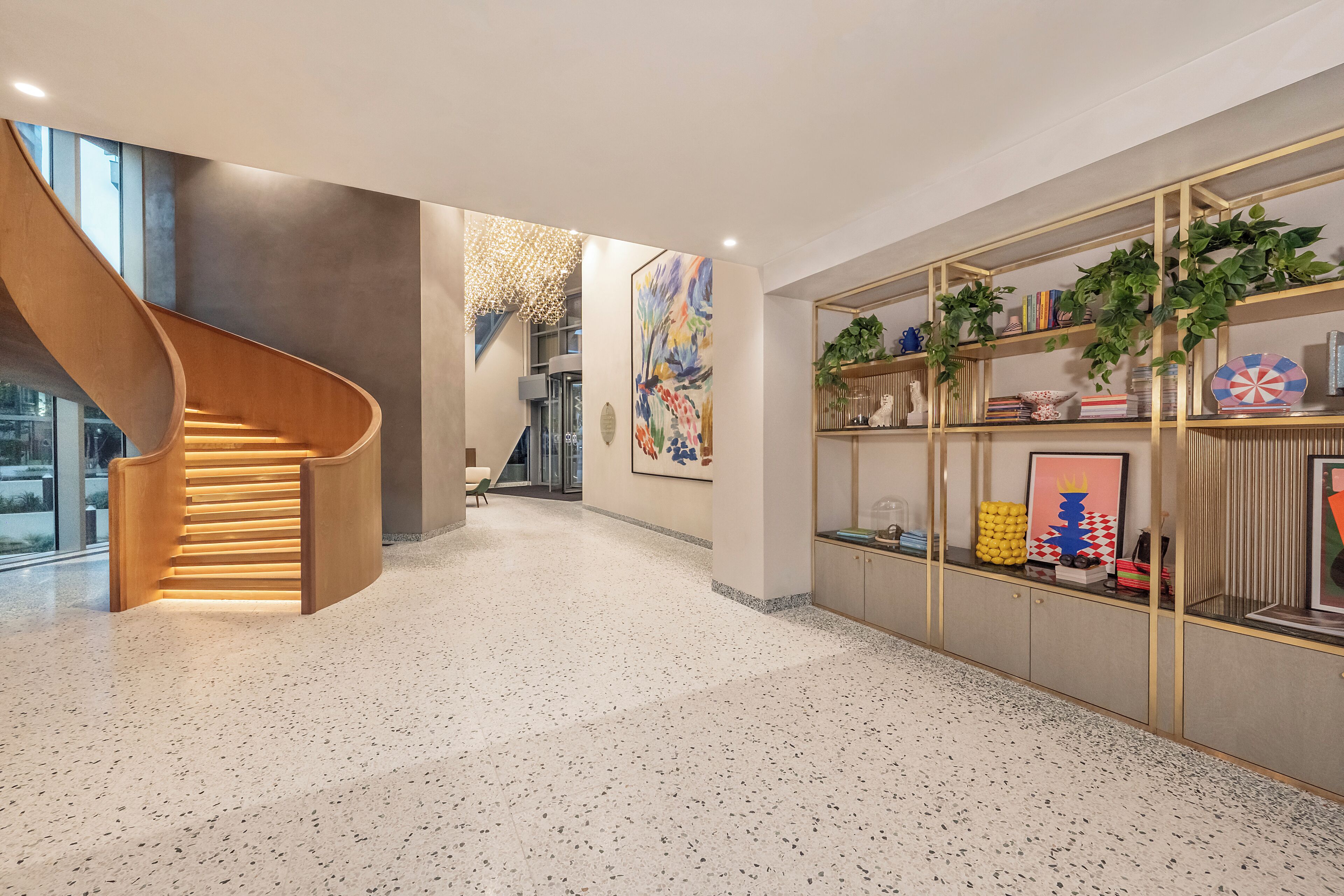 Un intérieur moderne avec un escalier en colimaçon, un couloir doté d’un sol à motifs et une bibliothèque agrémentée de divers objets décoratifs.