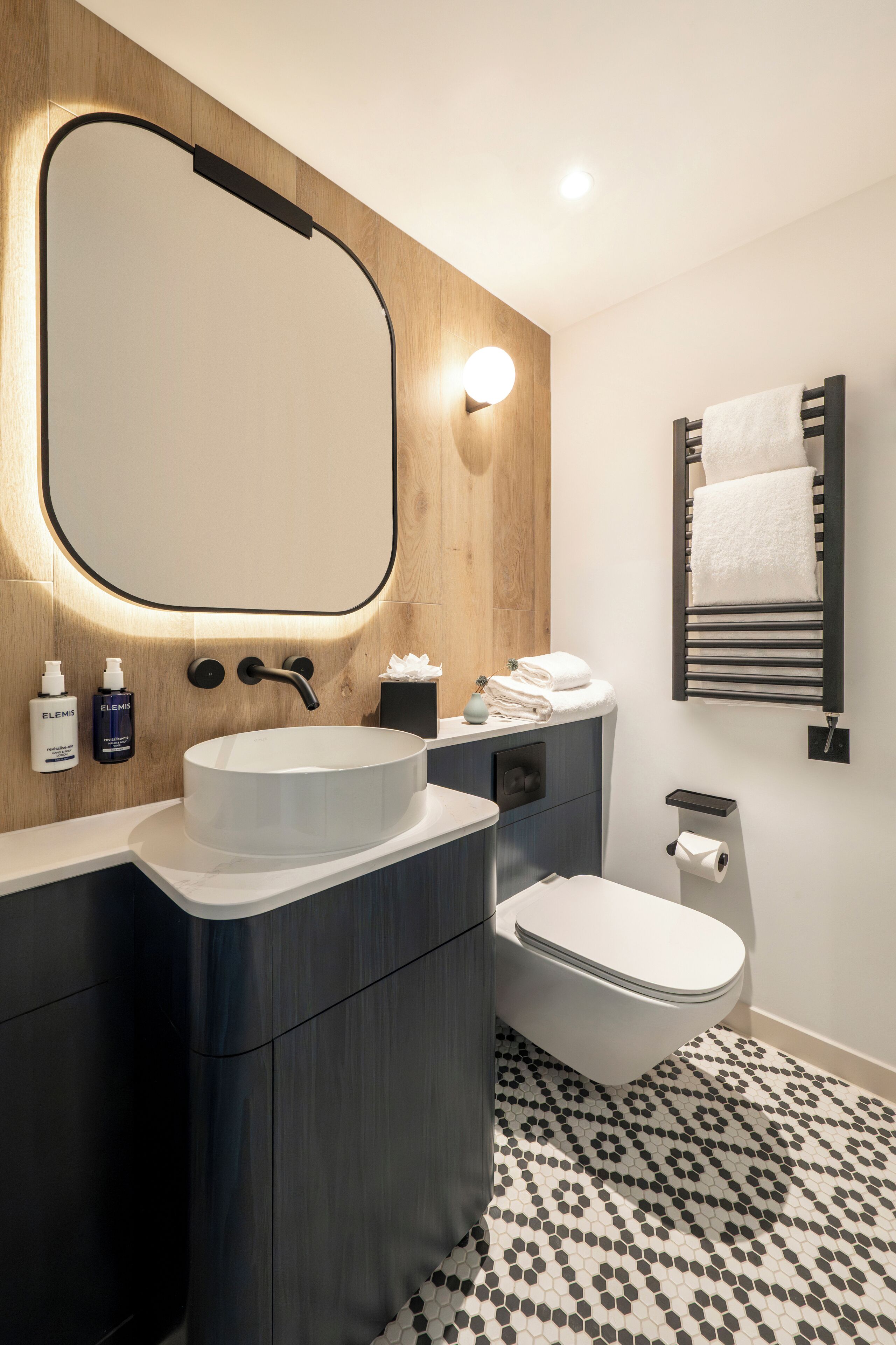 Een moderne badkamer met een houten wastafel, een rond wastafelblad, een toilet en een handdoekhouder.