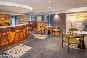 Eine moderne Bar mit gebogener Theke, mehreren Barhocker und einer Mischung aus grünen und orangen Stühlen.