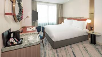 A hotel room with a bed, a desk with a coffee maker, a TV, and a mirror.