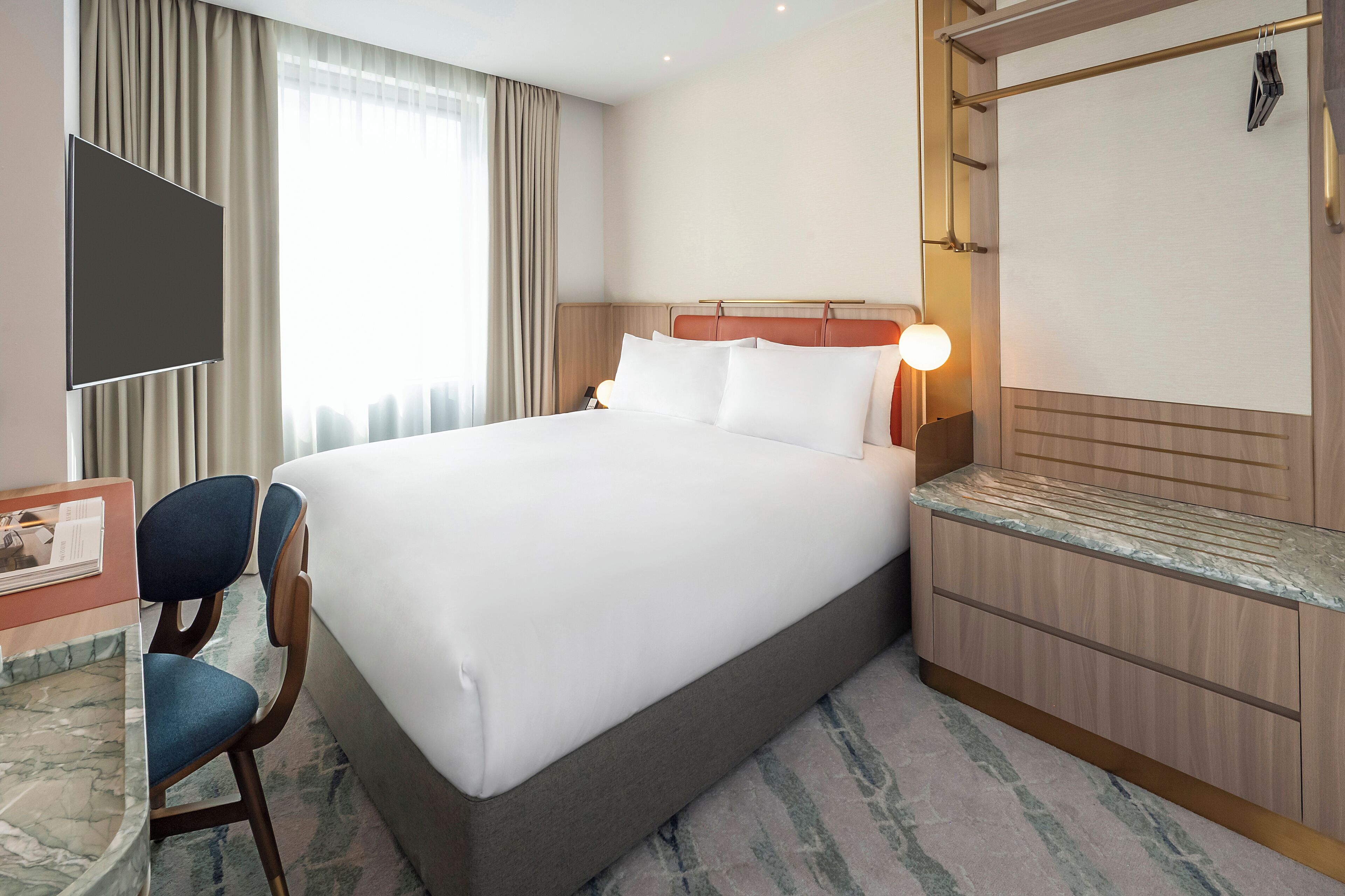 A hotel room with a large bed, a desk with a chair, a TV, and a window with curtains.