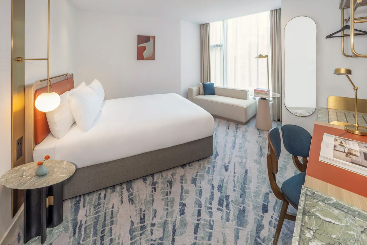 Une chambre d’hôtel avec un grand lit, un canapé, une petite table avec un vase, une chaise, un bureau avec une lampe et un grand miroir.