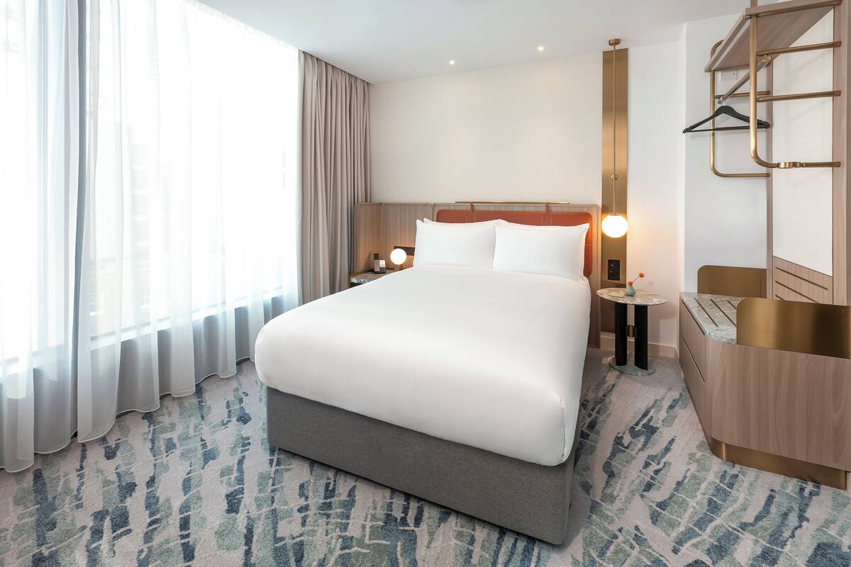 Une chambre d’hôtel avec un grand lit, une table de chevet avec une lampe, une armoire et une fenêtre avec des rideaux.