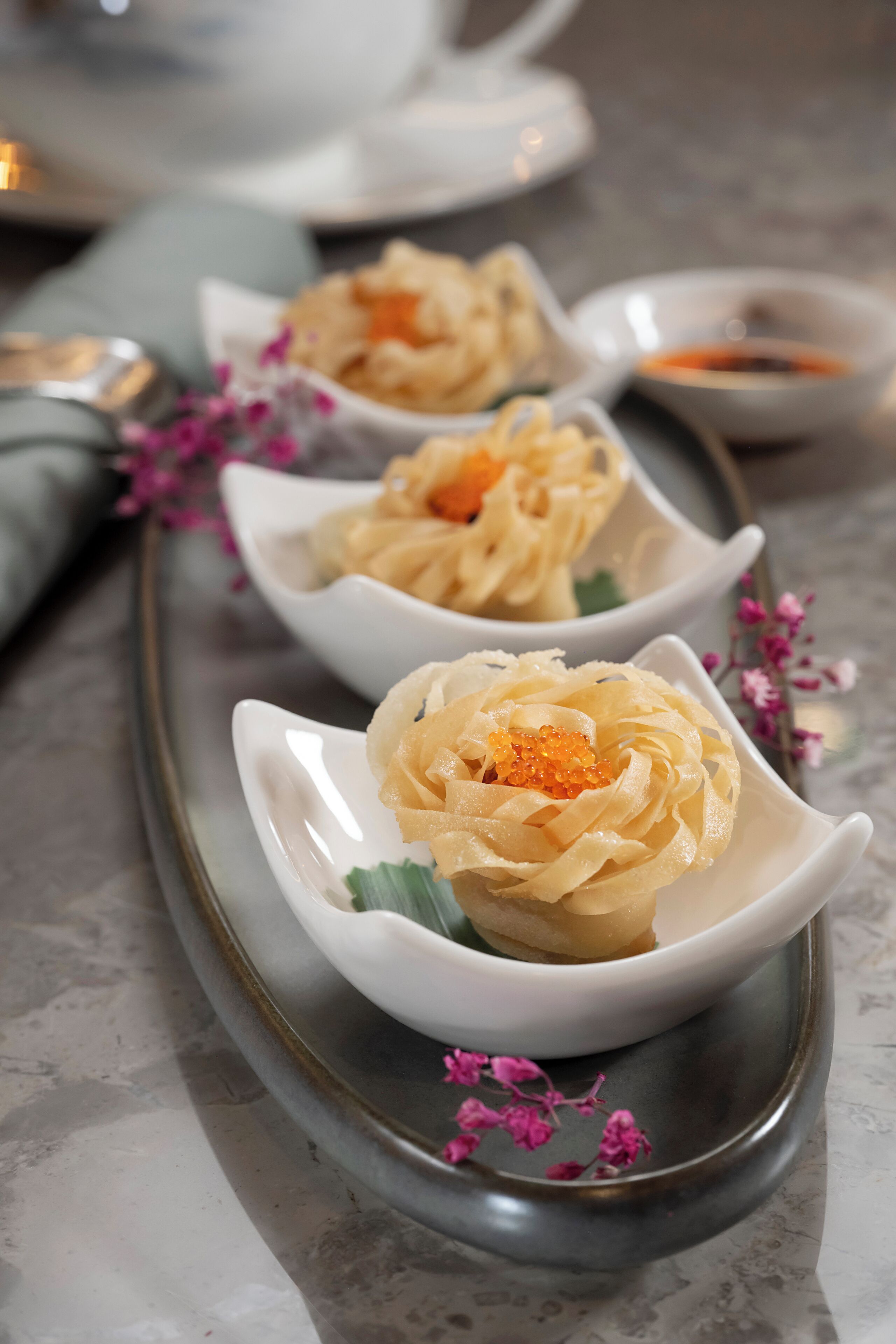 Three white bowls with a creamy substance and pink flowers on a gray tray.