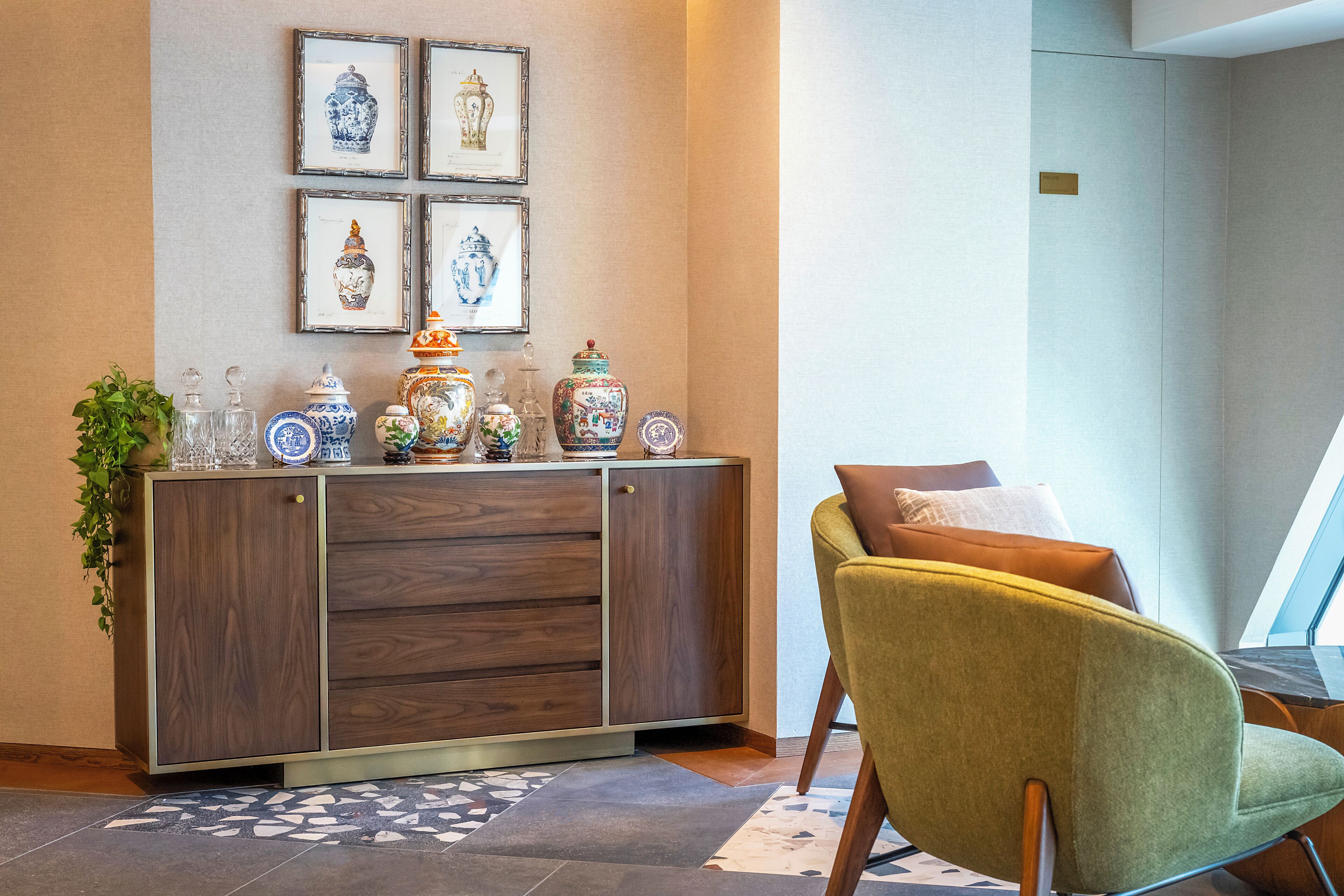 A modern room with a wooden cabinet displaying decorative items, a green armchair, and framed artwork on the wall.