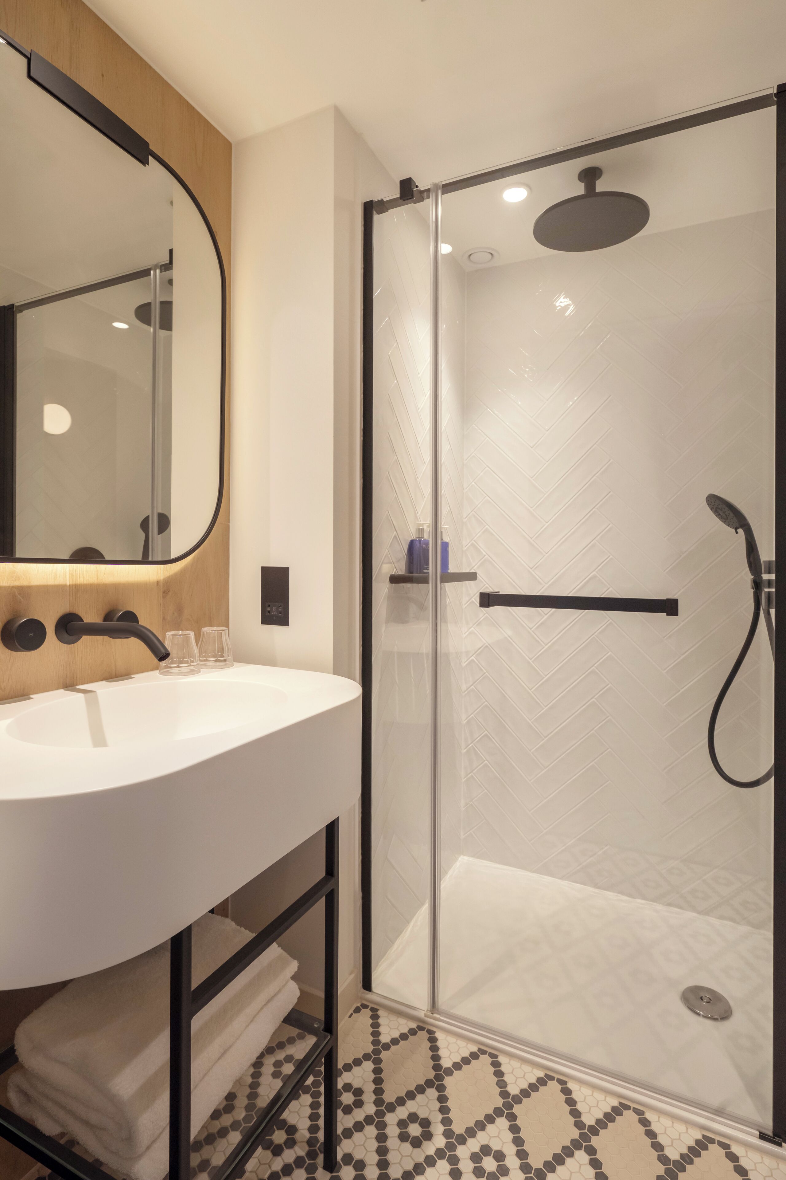 Un baño moderno con ducha de vidrio, lavamanos blanco y espejo con marco de madera.