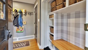 A hallway with a wooden bench, woven baskets on shelves, a coat rack with jackets, and a patterned rug.