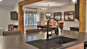 A modern kitchen with a central island, wooden beams, pendant lighting, and artwork on the walls.