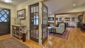 A spacious living area with a sofa, a coffee table, and a dining table with chairs. There is a TV mounted on the wall and a wooden floor.