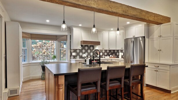 A modern kitchen with a large island, white cabinetry, and a stainless steel refrigerator.