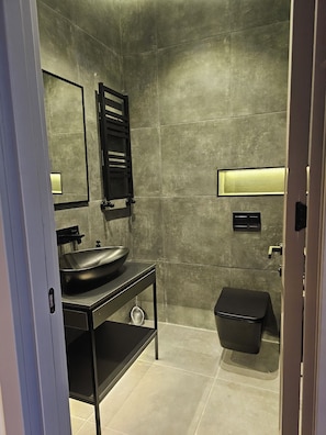 Ein modernes Badezimmer mit einem schwarzen Waschtisch, einem großen Spiegel, einem hängenden Handtuchhalter, einer Toilette und einem kleinen Ablagefach.