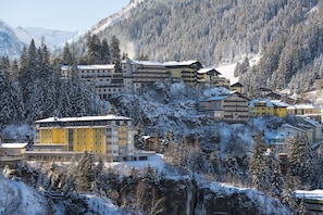 A snow-covered mountain resort with multi-story buildings, a ski lift, and a waterfall.