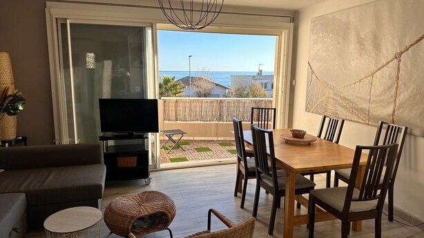 Una sala de estar con sofá, televisor y mesa de comedor con sillas. Tiene un balcón con vista al mar.