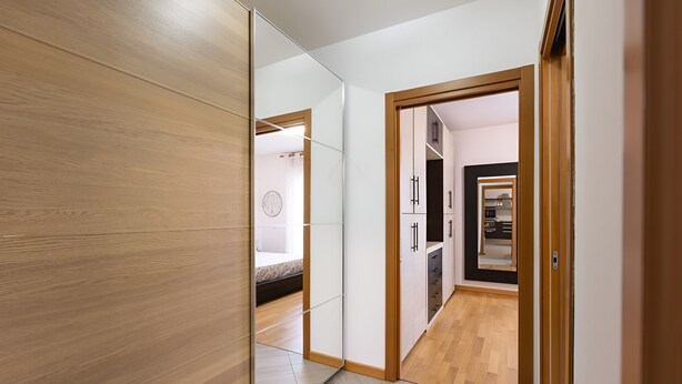 Un interior moderno con piso de madera, un armario espejado y una cocina visible a través de una puerta abierta.
