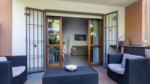 Un patio con mobiliario de mimbre, una pequeña mesa y un ventanal corredera que da a un espacio interior.