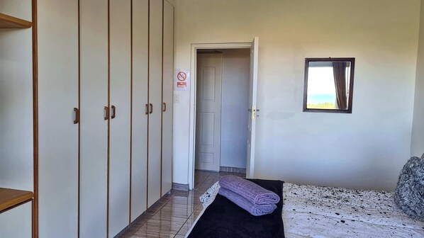 A bedroom with a bed, a window, a door, and a wardrobe.