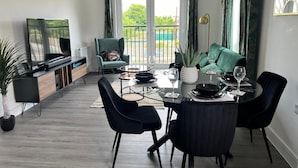 Ein modernes Wohnzimmer mit Essbereich, einem Fernseher und einem Balkon mit Vorhängen.