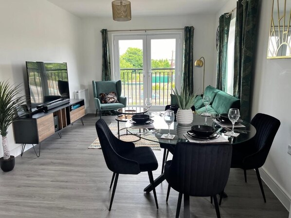 A modern living room with a dining area, a TV, and a balcony with curtains. - Modern 2 Bedroom Apartment (Sittingbourne)