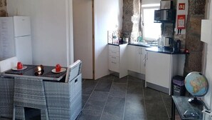 A compact kitchen with white cabinets, a stone wall, a dining area with wicker chairs, and a small table with red cups.