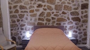 A bedroom with a stone wall, a bed with a quilted blanket, two bedside lamps, and a wooden chair.