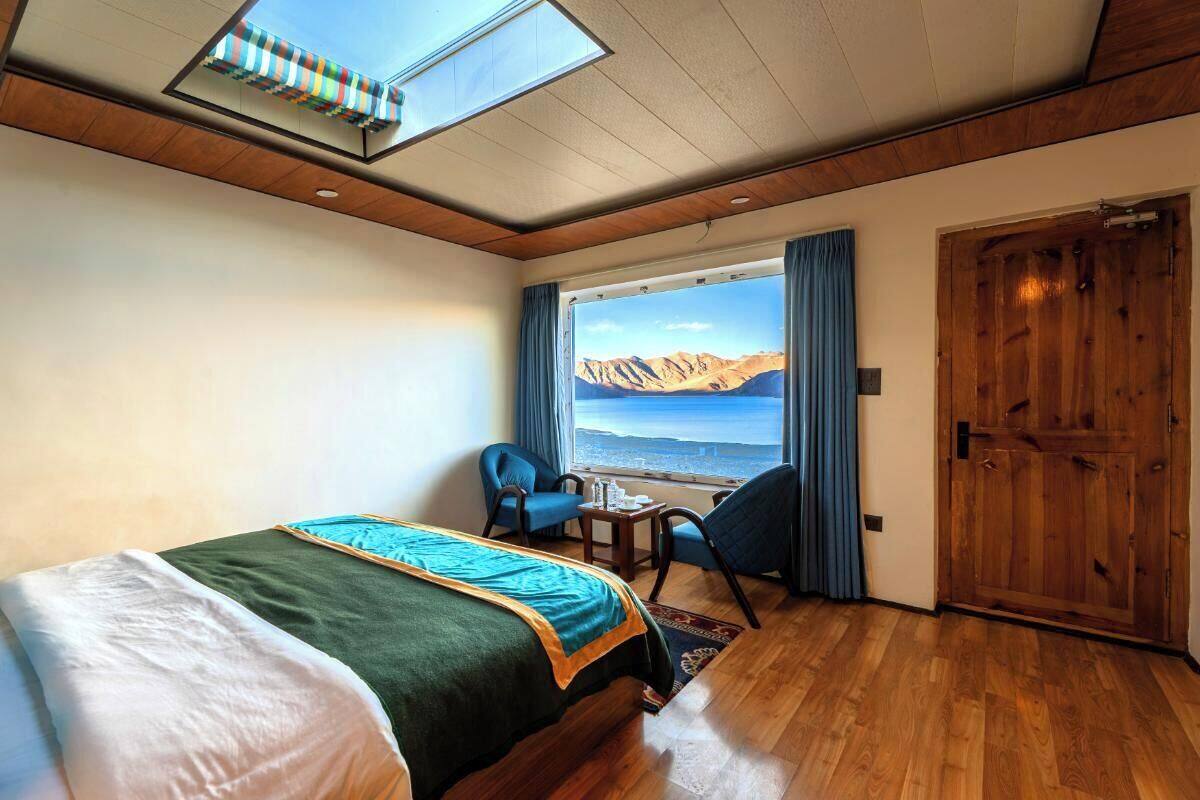 Habitación de hotel con cama, escritorio y vista a montañas a través de un ventanal grande.