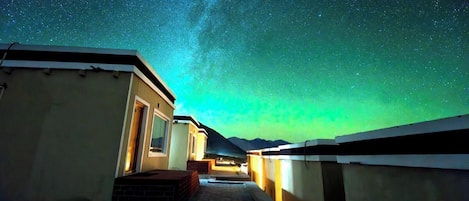 Un couloir donnant sur le ciel nocturne, qui mène à un bâtiment doté d’une porte et de fenêtres.
