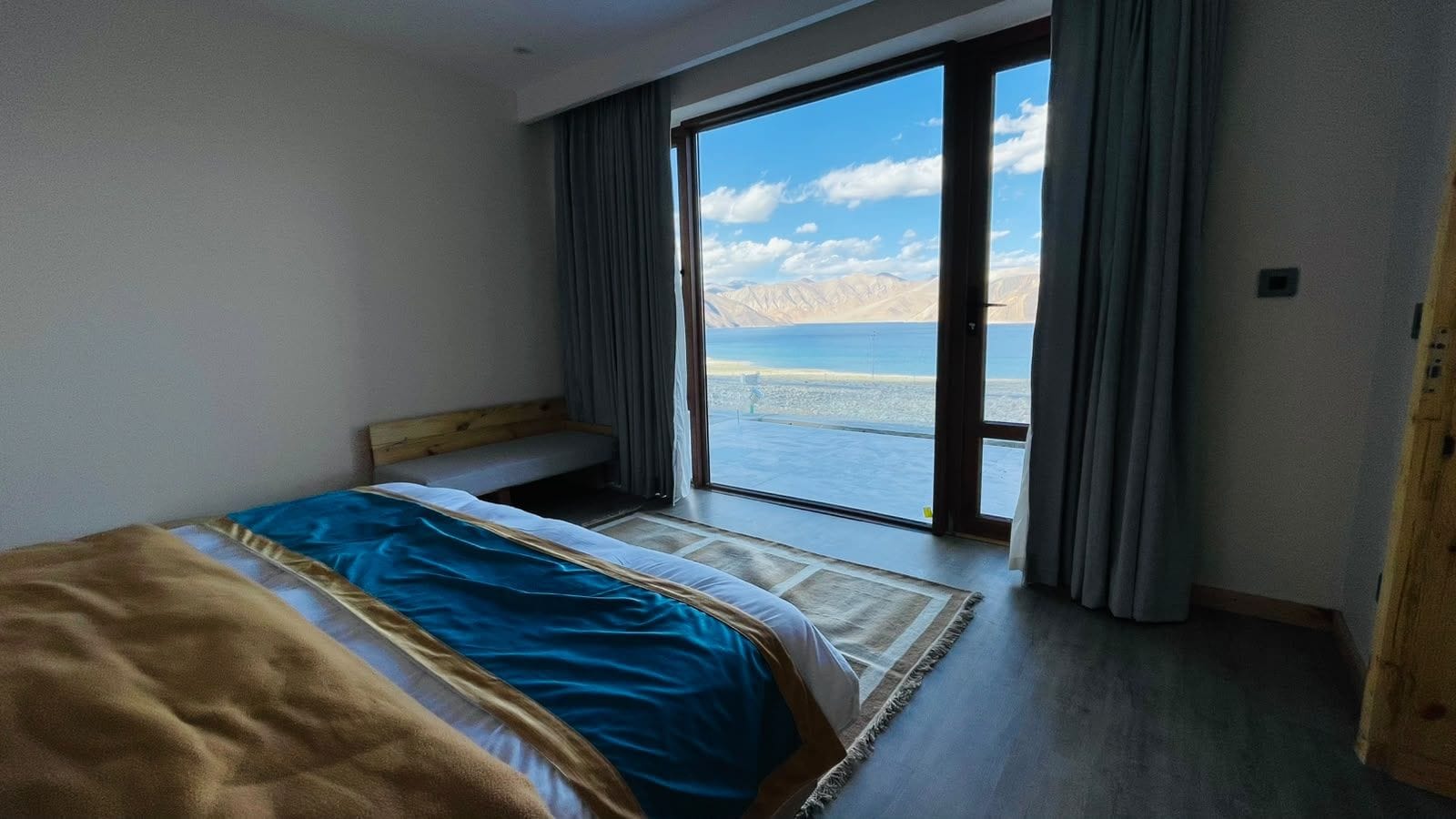 A hotel room with a bed, a bench, a large window, and a view of a body of water.