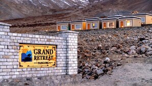 Schild für 'Grand Retreat' in Pangong, mit Bergblick und einer Reihe moderner, kompakter Ferienhäuser.