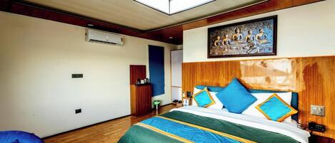 A hotel room with a large bed, a wooden headboard, a painting above the bed, a desk, and a chair.