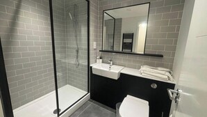 A modern bathroom with a glass shower enclosure, a white sink, and a black vanity. - Beaufort Park - 2 Beds - 2 Bathrooms (London)