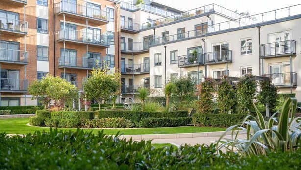 A modern apartment complex with multiple balconies, a well-maintained garden, and a variety of trees. - Beaufort Park - 2 Beds - 2 Bathrooms (London)