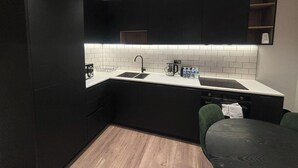 A modern kitchen with black cabinets, a white countertop, and a wooden floor. - Beaufort Park - 2 Beds - 2 Bathrooms (London)