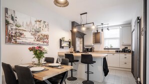 Eine moderne KĂĽche mit Kochinsel, Barhocker und Essbereich mit Tisch fĂĽr vier Personen.
