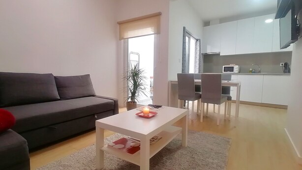 A living room with a sofa, a coffee table with a candle, and a view into a kitchen area. - CRISTIANO´S apartment with terrace in Alcochete (Alcochete)