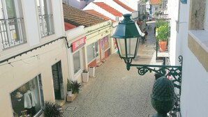A cobblestone street with buildings on either side, a shop with a 'Smile & Fone' sign, and a green street lamp. - CRISTIANO´S apartment with terrace in Alcochete (Alcochete)